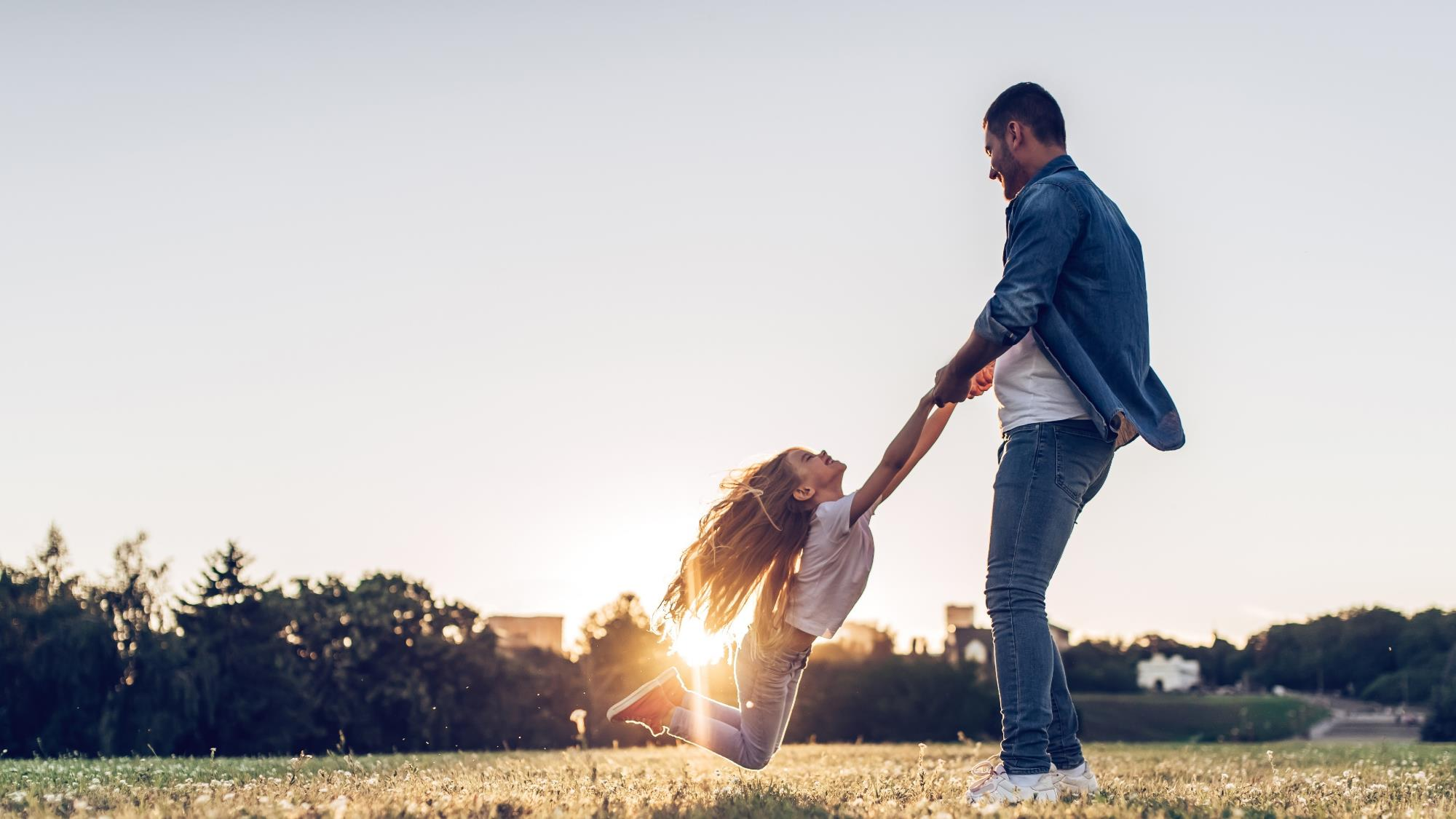 Father swinging his daughter at sunset in a grassy field
